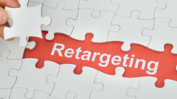 Gambar puzzle dengan bagian tengah berwarna merah bertuliskan 'Retargeting', sementara tangan seseorang sedang memasang satu kepingan puzzle putih yang masih kosong.