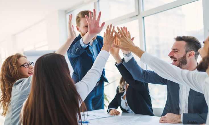 Karyawan kantor melakukan high five bersama di ruang kerja modern sebagai simbol semangat dan kolaborasi dalam meningkatkan employee engagement.