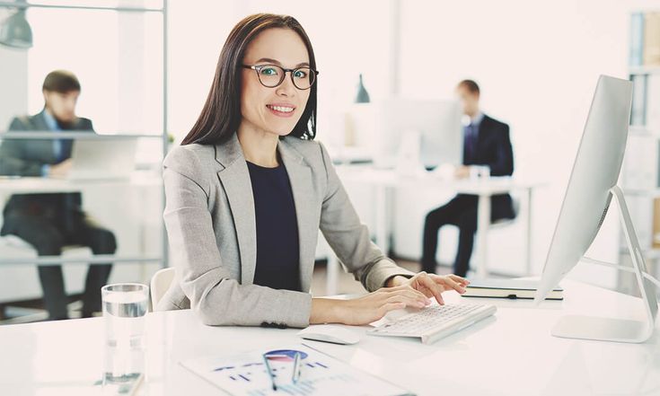 Seorang staf HR wanita sedang bekerja di depan komputer di kantor modern, menggambarkan manajemen data karyawan yang terorganisir dan profesional