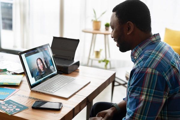 Seseorang sedang mengikuti uji sertifikasi kompetensi secara online dengan laptop dan dokumen di meja.