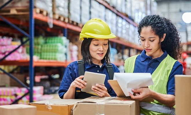 Pekerja wanita di supply chain warehouse sedang mengecek dokumen dan tablet, mencerminkan pentingnya sertifikasi profesi dalam green supply chain.
